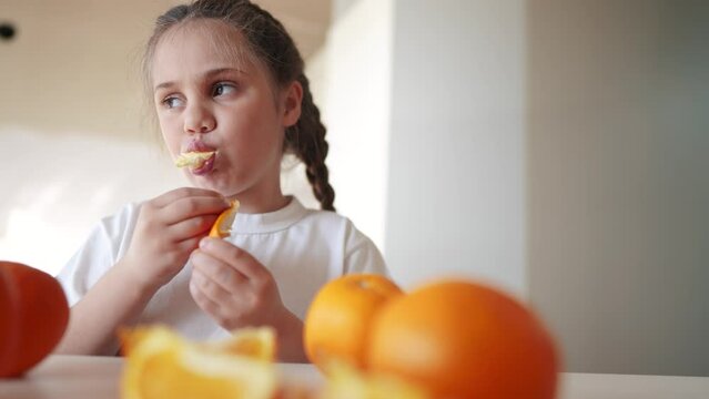 girl child eating oranges. happy family fruit healthy dream food kid concept. little girl daughter eating oranges at the table in the kitchen indoors. juicy fruits oranges are for a healthy diet
