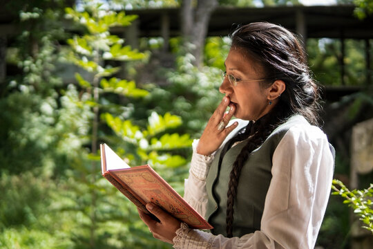 Profile portrait of a Latina woman dressed in traditional clothes, reading a book sitting in a park, with an expression of astonishment