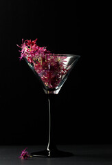 Cocktail glass filled with edible Turkish carnation flowers. Black background, vertical.