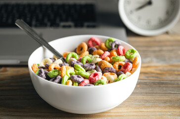 Colored breakfast cereals in a bowl and laptop, workplace breakfast, quick healthy breakfast in the office in the morning.