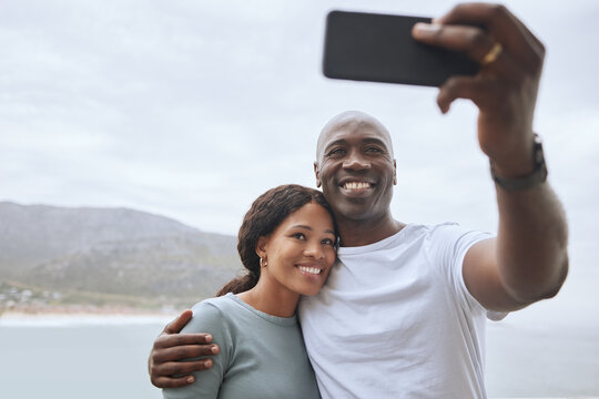 Handsome african american man and his beautiful wife taking selfies with a phone against a scenic seascape background. A black woman and her happy husband taking pictures while out hiking in nature