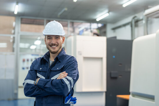 Male engineers standing and arms crossed at factory. Smiling technician wearing uniform and helmet safety operator CNC machine in workshop heavy metal industrial