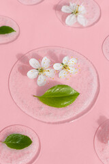 Obraz na płótnie Canvas Drops of transparent cosmetic gel or serum with white flowers and green leaves on a pink background. The concept of natural organic cosmetics.