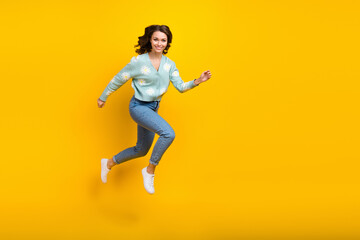 Fototapeta na wymiar Full length photo of young active model funny girl running jumping fast speed demonstrate her new stylish outfit isolated on yellow color background