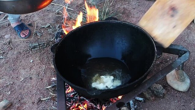 Woman throws pieces of cut yeast dough for baursaks from cutting board into cauldron with boiling oil. Preparation traditional bread of the Kyrgyz, Tajiks, Uzbeks