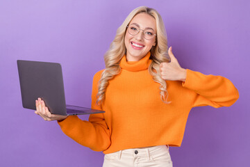 Photo of positive friendly girl stylish hairdo dressed orange sweater show like good job hold laptop isolated on purple color background