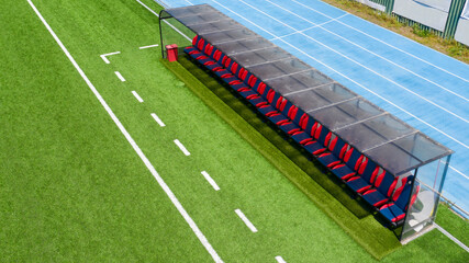Aerial closeup of the football benches on an empty synthetic grass soccer field. The seats on the...