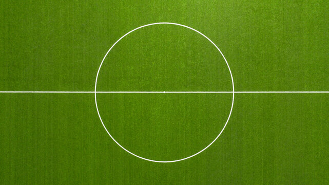 Aerial closeup of the midfield circle in an empty synthetic grass football field. Here the kick off is taken in a game of soccer.