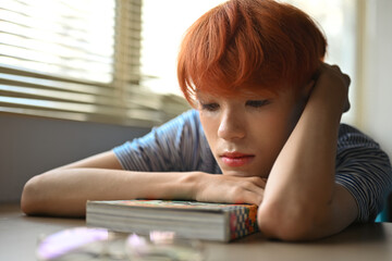 Cute teenage boy with bright colored hair looking bored when looking at the book.