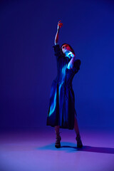 Portrait with one young beautiful woman in black dress looking up with dreaming face over dark studio background in neon light