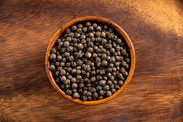 Black pepper seeds bowl. Up view studio shoot on wooden background.