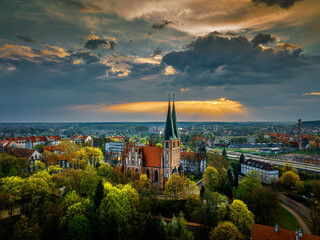 Olsztyn - Garrison Church of Our Lady Queen of Poland, park outside the castle from a bird's eye view. Above the church, the rays of the setting sun breaking through the clouds. Time of year - spring.