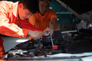 Both of auto mechanics are inspecting the engine of a customer's car being brought in for repair at a garage.