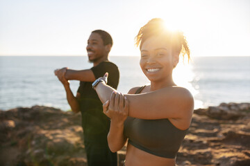 Positive millennial black couple in sportswear doing arm stretching, exercising, enjoy morning...