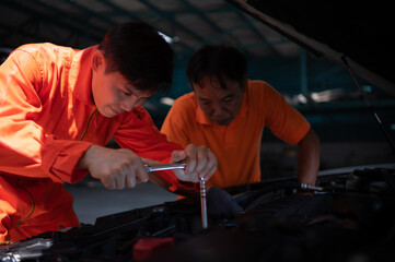 Both of auto mechanics are inspecting the engine of a customer's car being brought in for repair at a garage.