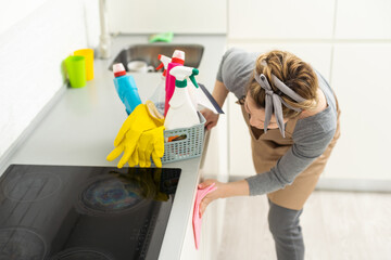 Young woman doing house chores. Woman holding cleaning tools. Woman wearing rubber protective yellow gloves, holding rag and spray bottle detergent. It's never too late to spring clean