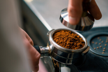 A professional barista in a coffee shop prepares ground coffee by tamping fresh ground coffee beans...