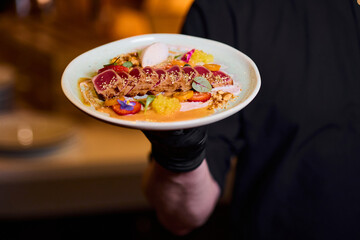 Close-up of a plate with a dish in the chef's hand. Fish restaurant, tuna dishes