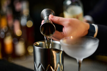 Close-up of the hands of a bartender who pours alcohol from a measuring cup into a shaker