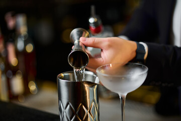Cocktail preparation at the bar. Bartenders prepare alcoholic cocktails. Measuring glass close-up in the hands of the bartender