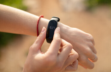 Young caucasian lady checks fitness tracker with empty screen, checks pulse, close up, unrecognizable
