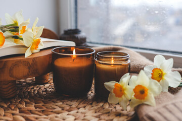 Two candles, daffodils and a book in a cozy home interior