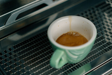 Pouring coffee flows from the machine into the cup making hot drink using the filter holder freshly...