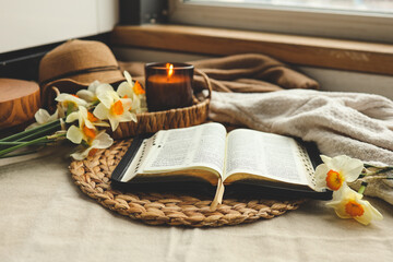 Open Bible with flowers and candles in a cozy home interior. Christian beautiful morning photography.