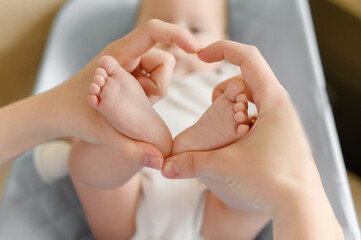 Feet of a child in mother's hands in the shape of a heart, close-up.Maternal love for her baby. Maternity leave, motherhood, happy childhood concept