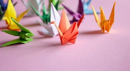 Paper cranes - origami on a pink background. Do-it-yourself jewelry. On the table are colored...