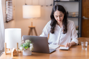 Attractive happy young Asian businesswomen at home, sitting at the desk, using a laptop computer, tablet and headphones having a video chat.