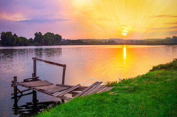 sunrise on the lake in the village. Beautiful setting sun. An old wooden fisherman's bridge. High quality photo
