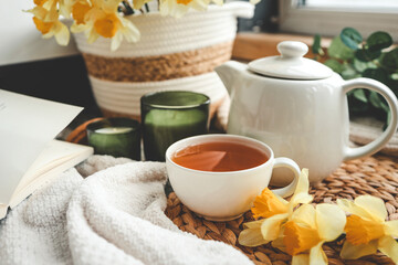 Cup of tea, candles, open book, basket with daffodils, spring aesthetic photo