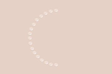 Drops of transparent gel or water are arranged in the shape of a not full circle. On a beige background.