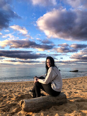 ragazza mora aspetta il tramonto seduta in un. tronco di legno di fronte al mare 