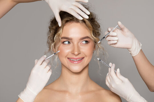 Beautiful lady getting facial injections by two cosmetologists, grey background