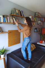 Young casual woman choosing a book to read during her leisure relaxing time at home.