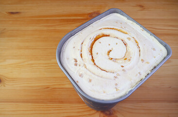 Tub of Delectable Salted Caramel Macadamia Nut Ice Cream Isolated on Wooden Table