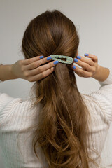 Fototapeta premium Caucasian woman touching a snap hair clip on her blond natural wavy hair with her blue short nails, spring vibes