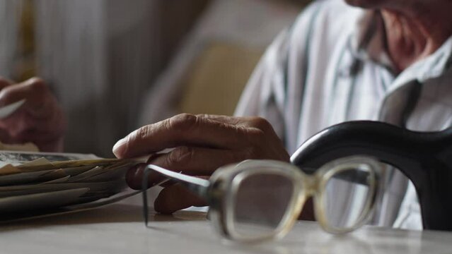a pensioner examines a stack of old family photos while sitting at a table with a walking stick. selective focus lifestyle of an elderly person. emotions of an old man, family tree