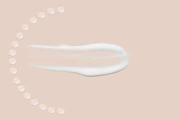 Drops of transparent gel and a dab of white cosmetic cream. On a beige background.