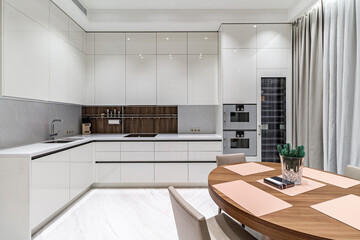 The interior of the kitchen and living room in light white colors with a table, chairs and a TV in a large free space.