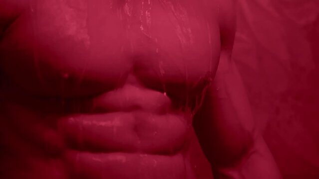 Young man muscular guy bodybuilder on which water pours Portrait of Sexy Male Falling rain or shower on a dark background. Concept: sport, strong healthy body and motivation.
