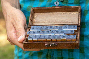 Man holding an old fashioned retro wooden box full of movable type rubber stamp alphabet letters...