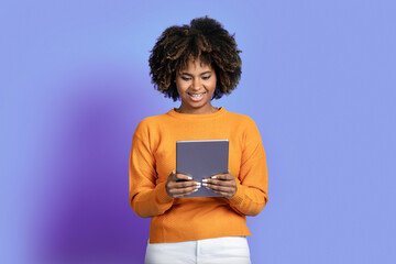 Smiling african american lady using modern pad on purple