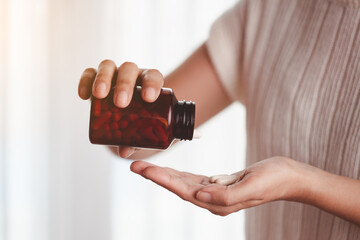 Asian woman's hand pouring medicines from a brown bottle