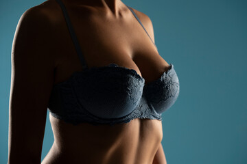 Close up on woman torso in the shadow. Blue bra and natural breasts cleavage on a blue background