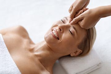 Smiling Middle Aged Woman Receiving Professional Anti-Aging Face Massage At Spa Center