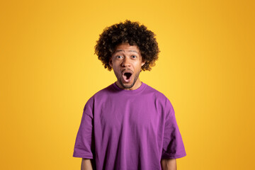 Positive excited shocked adult african american curly man in purple t-shirt with open mouth