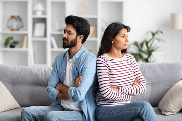 Upset young indian couple sitting on couch at home